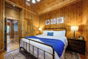 A wooden-paneled bedroom with a metal bed frame, two bedside tables with lamps, and a door leading to another room. - Classic! Away From It All! Hot Tub-Firepit-Arcade! (Broken Bow)