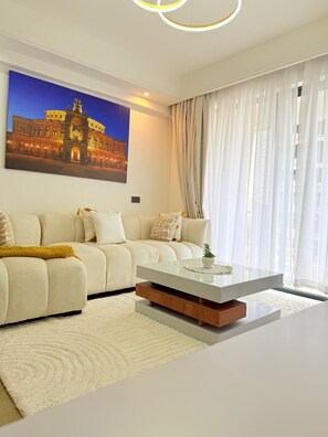 Una sala de estar moderna con un sofá, una mesa de centro de vidrio y un cuadro grande con la imagen de un edificio.