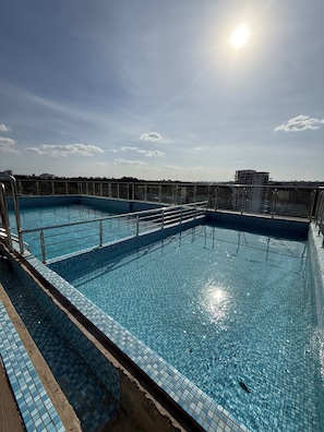 A rooftop swimming pool with clear blue water, surrounded by a metal railing, and a view of distant buildings under a clear sky. - Stylish 2BR Retreat in the Heart of Westlands (Nairobi)