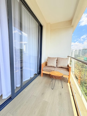 A balcony with a sofa and a round wooden table, a sliding glass door, and a view of buildings. - Stylish 2BR Retreat in the Heart of Westlands (Nairobi)