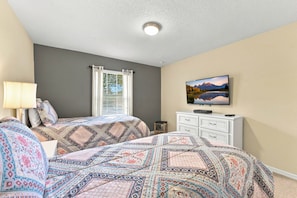 A bedroom with two beds, a window with blinds, a television on a dresser, and a painting on the wall. - Family 4BR Private Pool Resort Amenities (Kissimmee)