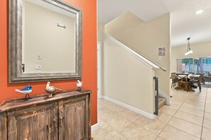Un pasillo con un aparador de madera y aves decorativas, una escalera con paredes color crema y un comedor con vistas.