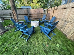 A backyard with a wooden fence, a tree, and a circular arrangement of blue chairs around a central table. - A quiet Oak Bluffs retreat steps from Circuit Avenue and Inkwell Beach. (Oak Bluffs)
