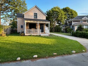 A two-story house with a front porch, a garage, and a well-maintained lawn. - A quiet Oak Bluffs retreat steps from Circuit Avenue and Inkwell Beach. (Oak Bluffs)