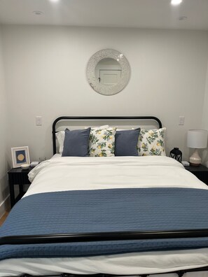 Un lit bien fait, avec une couette bleue, un coussin à motifs floraux et un autre coussin assorti, le tout sur une structure en métal noir.