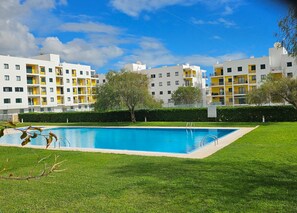 A swimming pool surrounded by well-maintained grass, with multi-story residential buildings in the background. - 1-Bedroom Apartment (Armação de Pêra)