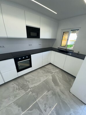A modern kitchen with white cabinets, a black countertop, and a built-in oven. - 1-Bedroom Apartment (Armação de Pêra)