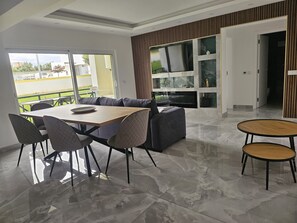 A modern living room with a dining table, chairs, a sofa, and a TV mounted on the wall. - 1-Bedroom Apartment (Armação de Pêra)
