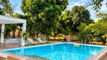 Una piscina rectangular con agua azul cristalina, rodeada por una terraza de madera y una pérgola blanca.