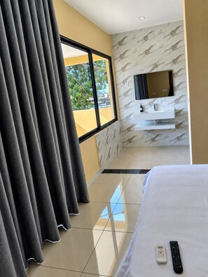A hotel room with a bed, a TV mounted on the wall, a bathroom with a mirror, and a window with curtains. - Quinta da Gabi (Viana)
