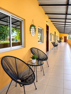 A corridor with black chairs and a potted plant, a wall with a sign, and windows with views of greenery. - Quinta da Gabi (Viana)