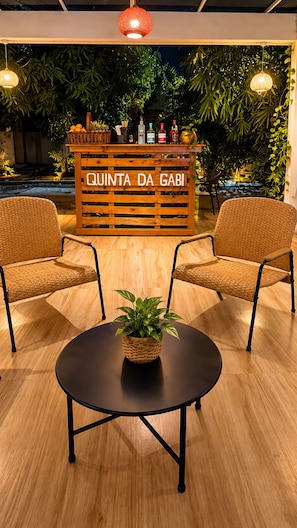 Una zona d'acollida amb un taulell de fusta amb la inscripció 'QUINTA DA GABI', dues cadires de vimet, una taula rodona amb una planta i un fons de vegetació i llums penjants.