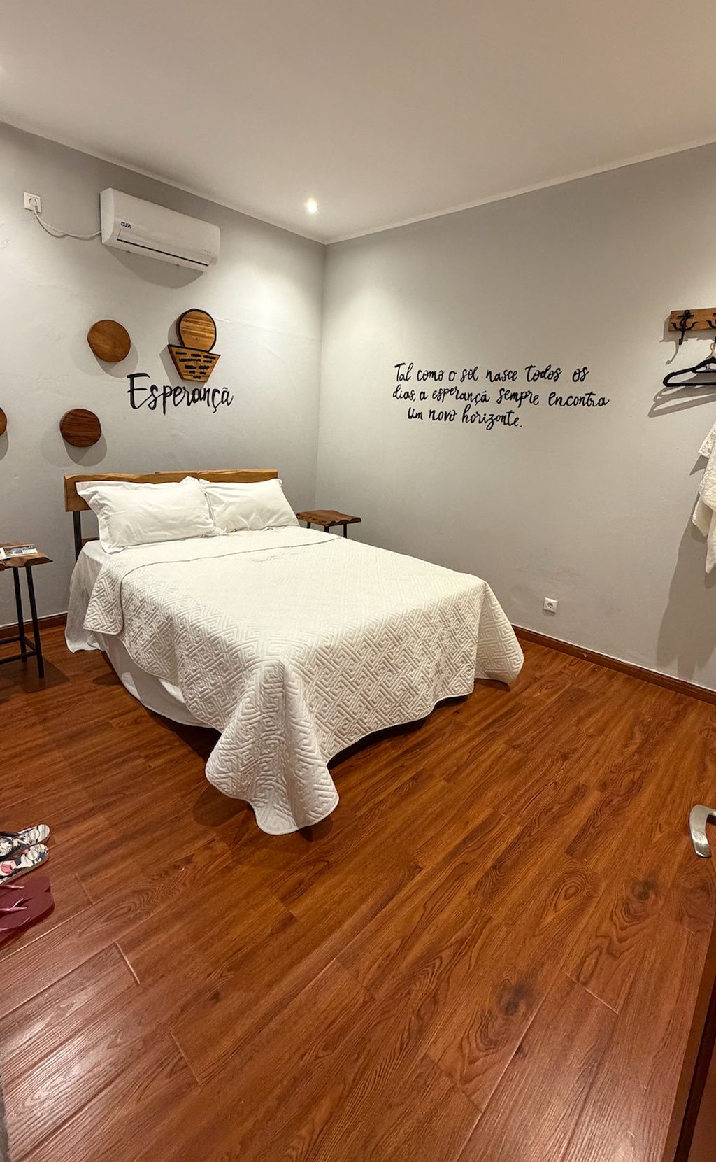 A bedroom with a bed, wooden floor, wall decor, and an air conditioning unit.