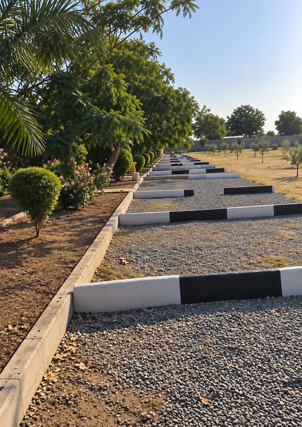 A pathway lined with neatly trimmed bushes and trees, leading to a gravel area.