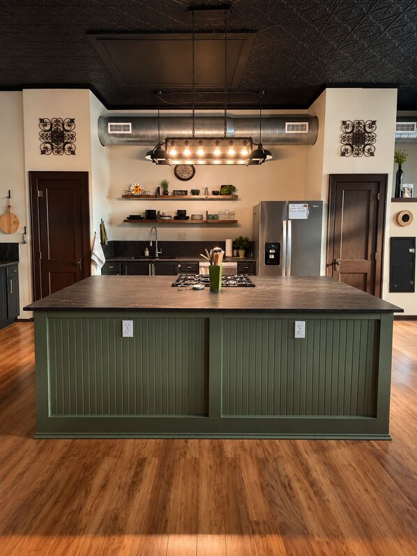 A kitchen with a central island, stainless steel appliances, and a hanging light fixture.