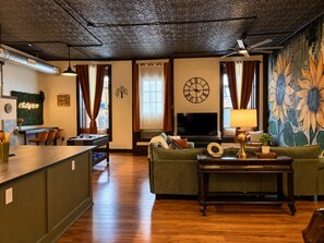 Ein Wohnzimmer mit Holzboden, einem grünen Sofa, einem Fernseher und einer Wanduhr.