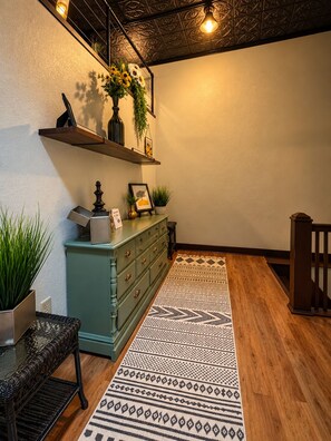 Ein Zimmer mit Holzboden, einem gemusterten Teppich, einem grünen Schminktisch und einem an der Wand befestigten Regal mit Dekoration.