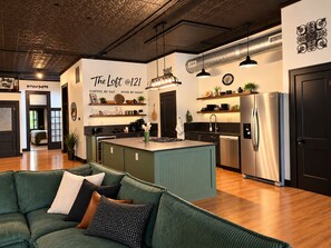 A modern kitchen with a central island, stainless steel appliances, and a dining area with a green sofa.