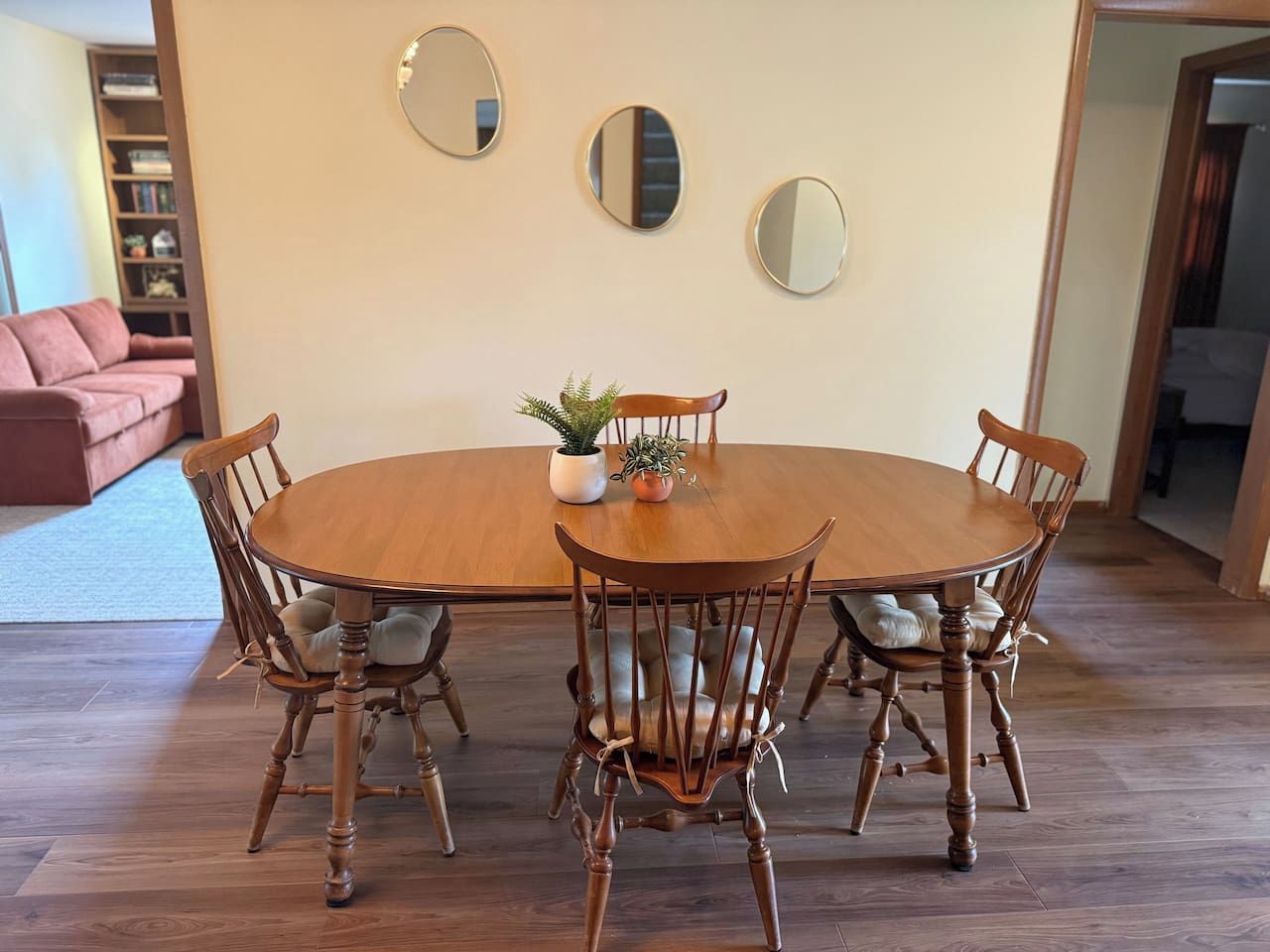 Uma mesa de jantar com quatro cadeiras, um vaso de planta e três espelhos na parede.