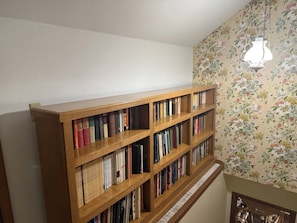 Une bibliothèque en bois remplie de livres, un papier peint à motifs floraux sur le mur et un luminaire suspendu.
