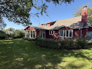 A red house with a chimney, surrounded by a well-maintained lawn and dense foliage. - The Capsule: 60s Charm + Private Movie Theater (Sioux Falls)