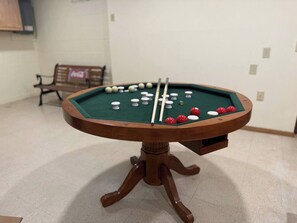 Una mesa de billar con bolas y tacos, un banco y una pared con un letrero.