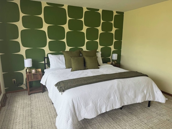 A neatly made bed with a white comforter and a dark throw blanket, positioned against a wall with a geometric pattern. - The Capsule: 60s Charm + Private Movie Theater (Sioux Falls)