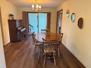 Une salle à manger avec une table ronde en bois, six chaises, un piano et un lustre.