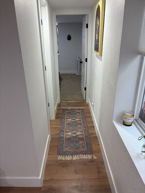 A hallway with a patterned rug, a door leading to another room, and a window with a jar on the sill. - Cozy basement 1B1B apt. in Barnum neighborhood, 10mins from city & mtns (Denver)