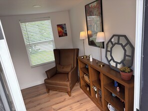 Ein Zimmer mit einem braunen Sessel, einem Holzschreibtisch mit Lampen, einem Spiegel und einem Fenster mit Jalousien.