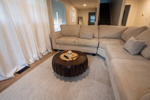 A living room with a sectional sofa, a round coffee table, and a large window with curtains. - 4BR Modern Farmhouse, Golf Views  Sleeps 10 (Belton)