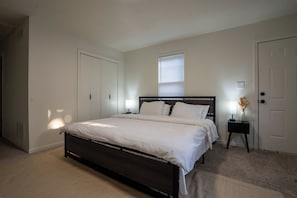 A bedroom with a bed, a nightstand, a window with blinds, and a door. - 4BR Modern Farmhouse, Golf Views  Sleeps 10 (Belton)