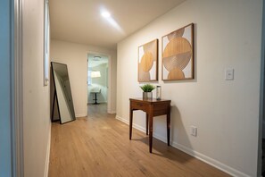 A hallway with wooden flooring, a mirror, a table with a plant, and two wall-mounted artworks. - 4BR Modern Farmhouse, Golf Views  Sleeps 10 (Belton)