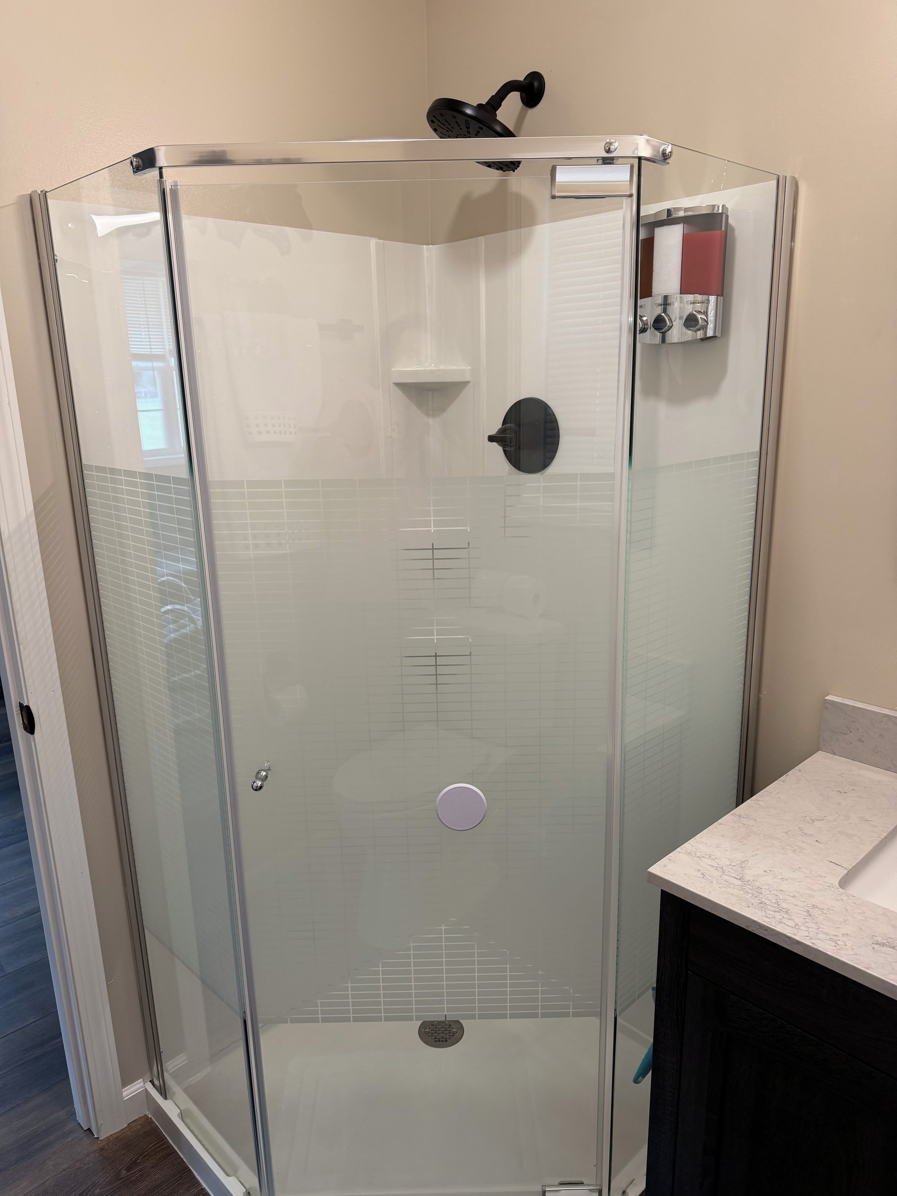 A glass-enclosed shower stall with a handheld showerhead, a control panel, and a wall-mounted faucet.