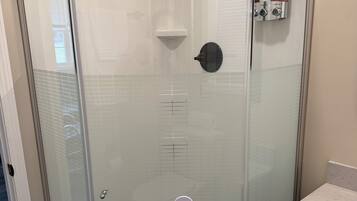 A glass-enclosed shower stall with a handheld showerhead, a control panel, and a wall-mounted faucet.