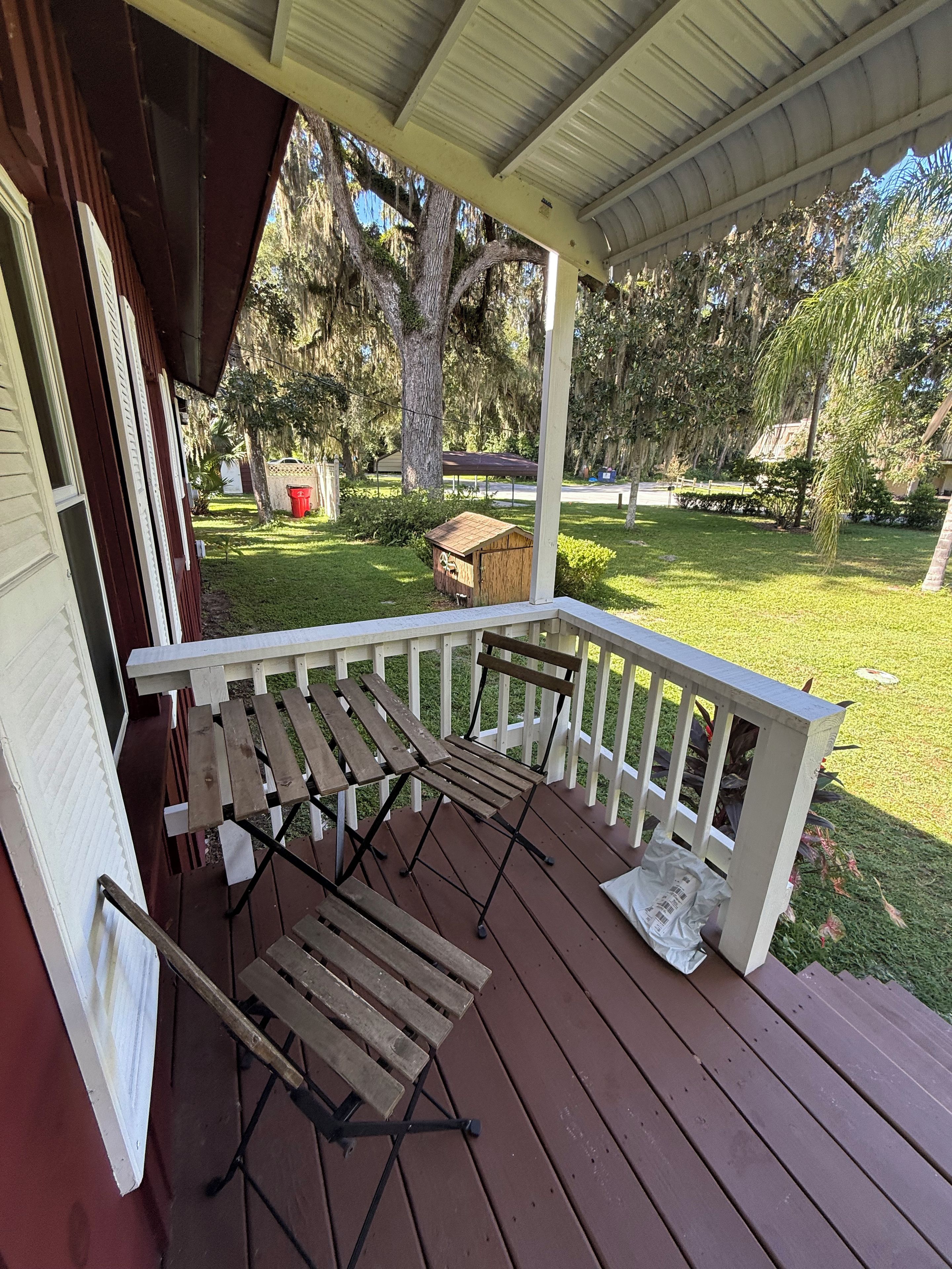 A covered porch with a wooden bench and a table, surrounded by a white railing.