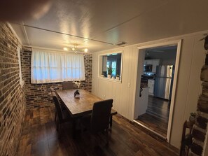 A dining area with a wooden table and chairs, a brick wall, and a view into the kitchen. - Lake Panasoffkee retreat 2brm/2bath with boat parking (Lake Panasoffkee)