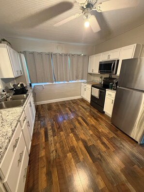 A kitchen with white cabinets, a stainless steel refrigerator, a microwave, and a wooden floor. - Lake Panasoffkee retreat 2brm/2bath with boat parking (Lake Panasoffkee)