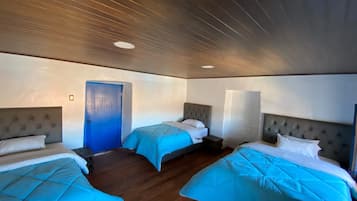 Habitación de hotel con tres camas, piso de madera y puerta azul.