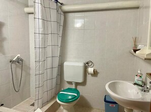 A bathroom with a shower, toilet, sink, and a trash bin. - Cozy Apartments Drazica 4 (Novalja)
