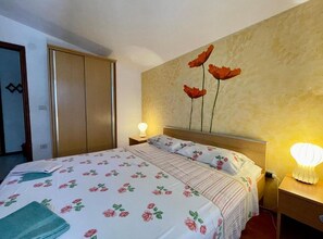 A hotel room with a bed, a nightstand, a wall-mounted lamp, and a wardrobe. - Cozy Apartments Drazica 4 (Novalja)