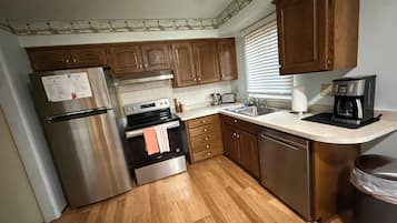 Una cocina con gabinetes de madera, electrodomésticos de acero inoxidable, una encimera y un ventanal con persianas.