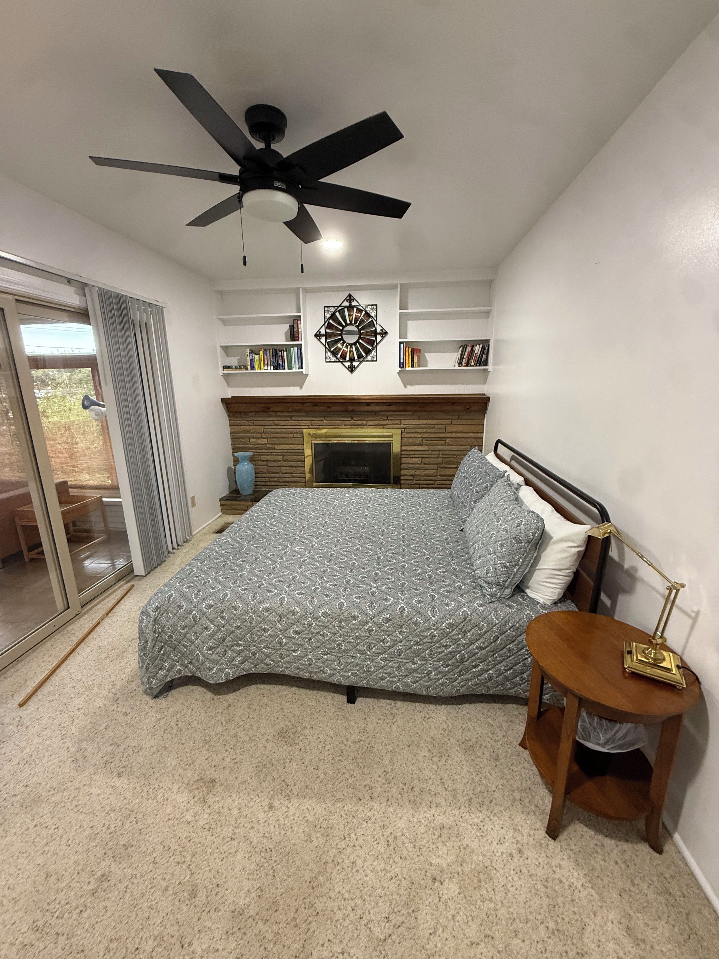 Un dormitorio con cama, mesita de noche, ventilador de techo, chimenea y estantería.
