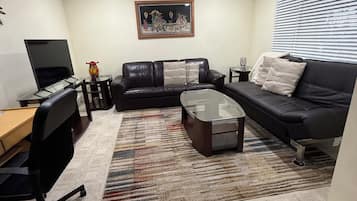 A living room with a black leather sofa, a glass coffee table, a black office chair, a TV, and a framed picture on the wall.