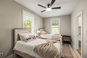 Ein Schlafzimmer mit zwei Betten, einem Deckenventilator und großen Fenstern.