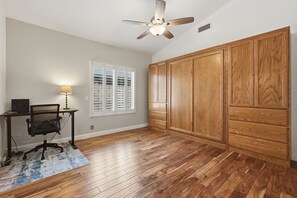 A room with hardwood flooring, a ceiling fan, a desk with a chair, a window with blinds, and a wooden wardrobe. - Charming Gilbert Home: Primary Suite, Flex 2nd BR/Office, Near Park & Downtown (Gilbert)