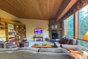 A cozy living room with a fireplace, a television, and a large window. - 4BR Big Sky Condo with Private Hot Tub & Sauna (Big Sky)