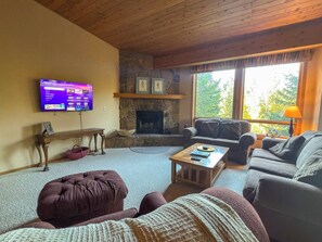 A cozy living room with a stone fireplace, comfortable seating, and a flat-screen TV mounted on the wall. - 4BR Big Sky Condo with Private Hot Tub & Sauna (Big Sky)