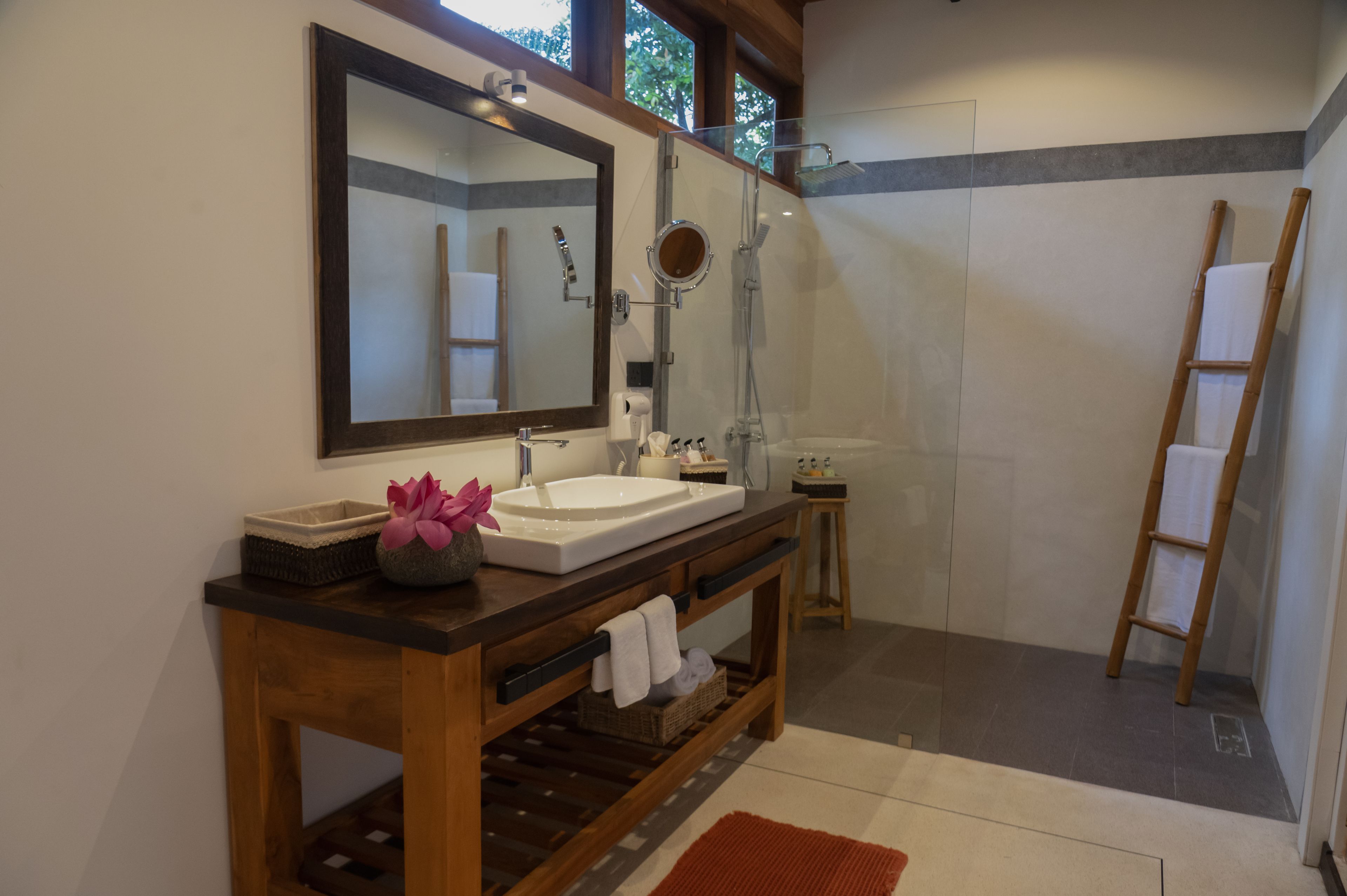 Un baño con un espejo grande, un lavabo, una zona de ducha y una escalera de madera.