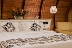 Un dormitorio con techo de madera, una cama con ropa de cama estampada, una mesita de noche con una lámpara y una silla.